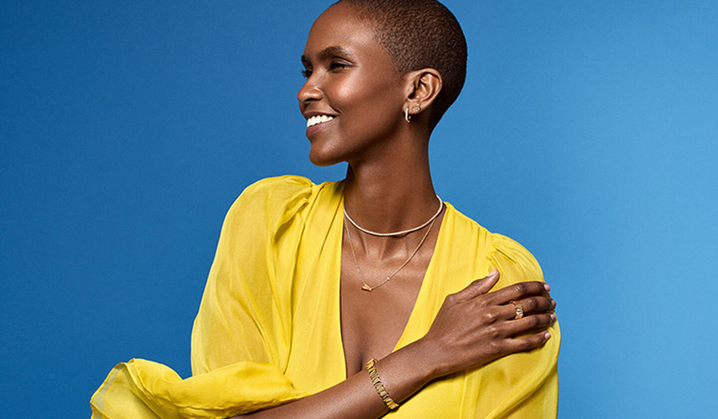 A woman wearing yellow gold and diamond jewellery from Birks on a blue background.